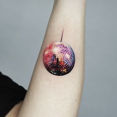 a woman's arm with a colorful disco ball tattoo on it