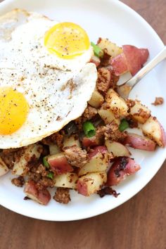 two fried eggs on top of potatoes in a white bowl with a fork next to it