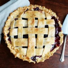 a pie sitting on top of a wooden table next to a fork and spoons