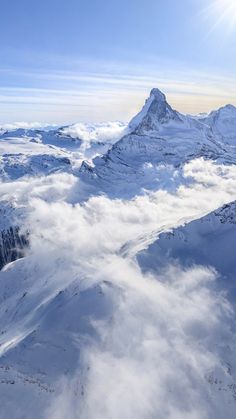 the view from an airplane looking down at snow covered mountains and clouds in the foreground