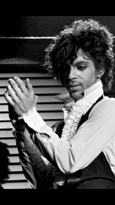 a man with curly hair wearing a vest and holding his hands together in front of him