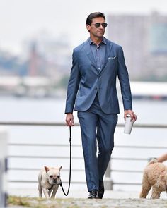 a man in a blue suit walking two dogs on a leash and holding a coffee cup