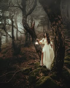 a woman in a white dress is standing next to a tree and holding a lantern