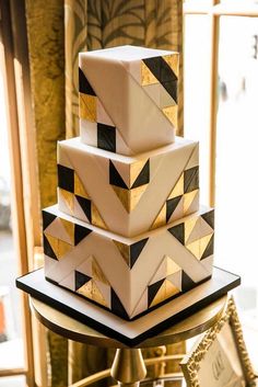 a three tiered cake with black and white designs on it's sides, sitting on a gold pedestal