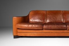 a brown leather couch sitting on top of a white floor next to a gray wall