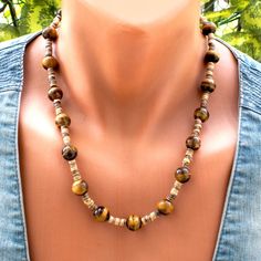 Make a bold statement with this Chunky Tiger Eye Bead Necklace. Crafted with striking 12mm Tiger Eye beads and accented with coconut beads, this large stone necklace exudes confidence and style. Each bead showcases the unique patterns and colors of Tiger Eye, making every piece one-of-a-kind. Finished with a durable steel wire and clasp, this statement necklace is perfect for adding a touch of natural beauty to any outfit. ------------------------------------------------------------------ Check Big Tiger, Heishi Necklace, Tiger Eye Jewelry, Tigers Eye Necklace, Large Stone, Outfit Check, Necklace Chunky, Blue Tigers Eye, Tiger Eye Beads