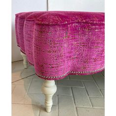 an upholstered bench with pink fabric and beading on the legs, in front of a white wall