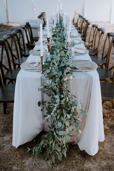 a long table with white linens and greenery is set up for an outdoor dinner