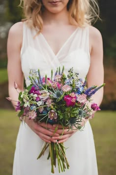 a woman in a white dress holding a bouquet of purple and blue flowers on her wedding day