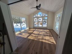 an empty room with wood floors and a ceiling fan in the corner, looking out onto a snowy yard