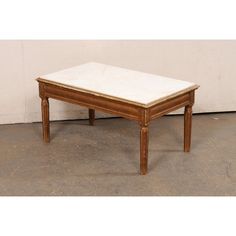 an old wooden table with marble top on concrete floor in front of a white wall