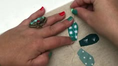 a woman's hands with red and green manicures on her nails next to a piece of fabric