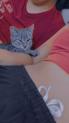 a woman laying on top of a bed with a gray cat next to her stomach