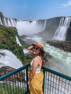 a woman standing in front of a waterfall with a hat on her head and sunglasses on