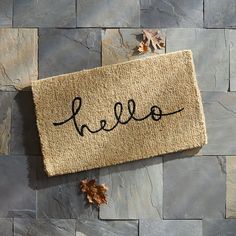 a door mat with the word hello written on it next to some leaves and rocks