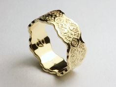 a gold ring with an intricate design on the outside and inside, sitting on a white surface