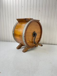 an old wooden barrel on a stand with a hook in the middle and a white wall behind it