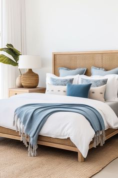 a bed with blue and white pillows on top of it next to a plant in a vase