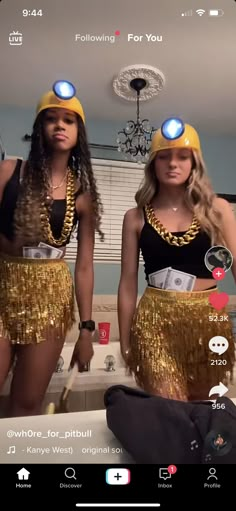 two women wearing gold sequins in front of a mirror with lights on them