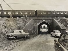 an old black and white photo of cars going into a tunnel with a train in the background