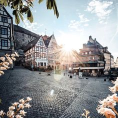 the sun shines brightly in an old town square with flowers on the cobblestone