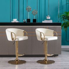 two white and gold bar stools in front of a blue wall