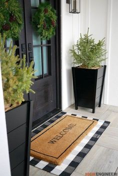 two black planters with evergreens and pine cones are on the front door mat