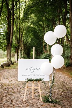 a sign that is on top of a wooden easel in the woods with balloons attached to it