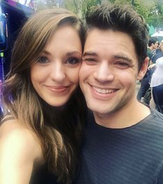 a man and woman are posing for a photo in front of an outdoor area with people