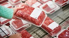 a person holding up a package of ground beef in front of other packaged meats