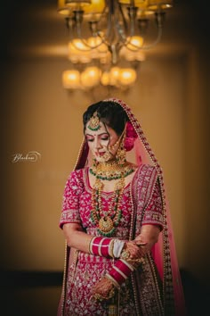 a woman in a red and gold bridal outfit standing under a chandelier