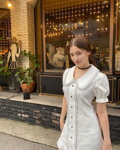 a woman standing in front of a store window wearing a white dress and black choker necklace