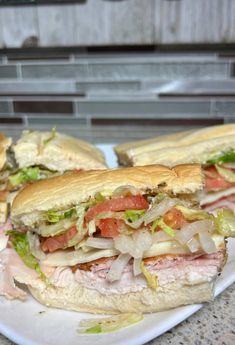 two sub sandwiches with meat, lettuce and tomato on a white platter