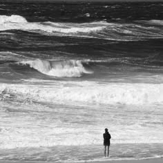 a person standing on the beach looking out at the ocean with waves coming in to shore