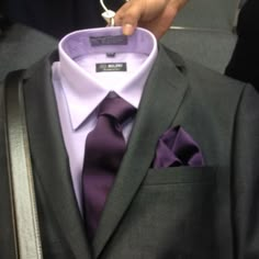 a man in a suit and tie is holding his purple shirt with the tag on it