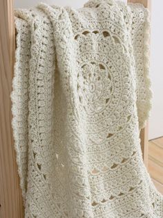 a white crocheted blanket hanging on a wooden rail with wood slats in the background