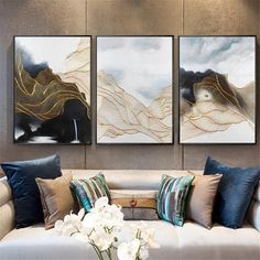 three paintings on the wall above a couch in a living room with white and blue pillows