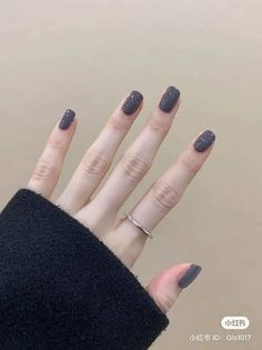 a woman's hand with grey nail polish and ring on her left thumb, in front of a beige background