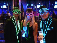 three people wearing neon glasses and hats pose for a photo with drinks in their hands