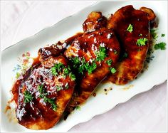 three pieces of meat covered in sauce and parsley on a white serving platter