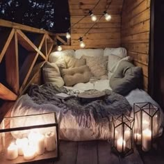 a bed sitting on top of a wooden floor covered in pillows and blankets next to lit candles