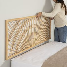 a woman placing a bamboo headboard on a bed