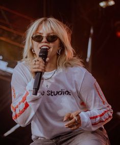 a woman with sunglasses on holding a microphone in front of her face and singing into the microphone