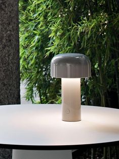 a table lamp sitting on top of a white table next to a plant covered wall