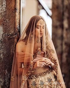 a woman in a wedding dress standing next to a wall with a veil on her head