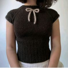 a woman wearing a brown sweater with a bow at the neck and white shorts underneath