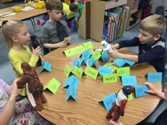 several children sitting around a table playing with toy animals and sticky notes on the table