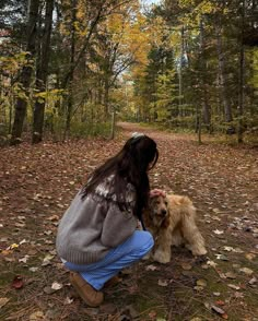 a woman kneeling down next to a dog on a forest floor with leaves all over the ground