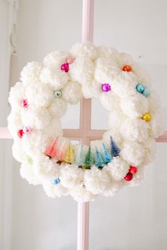 a white wreath hanging from the side of a pink cross with colorful beads on it