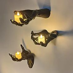 three candles are lit in the shape of hands and feet on a white wall with shadows